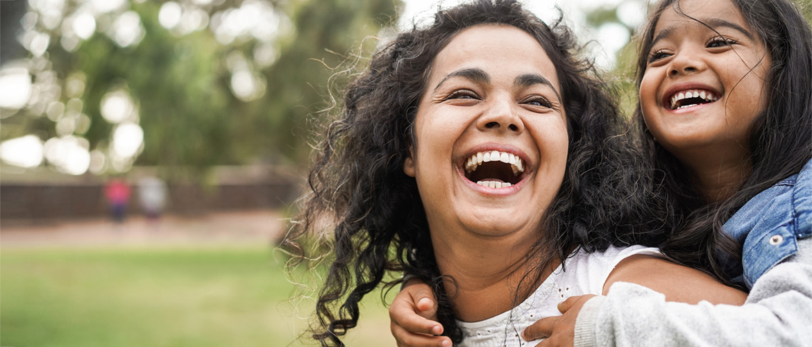 Latina girl rides on woman's shoulders outside. 