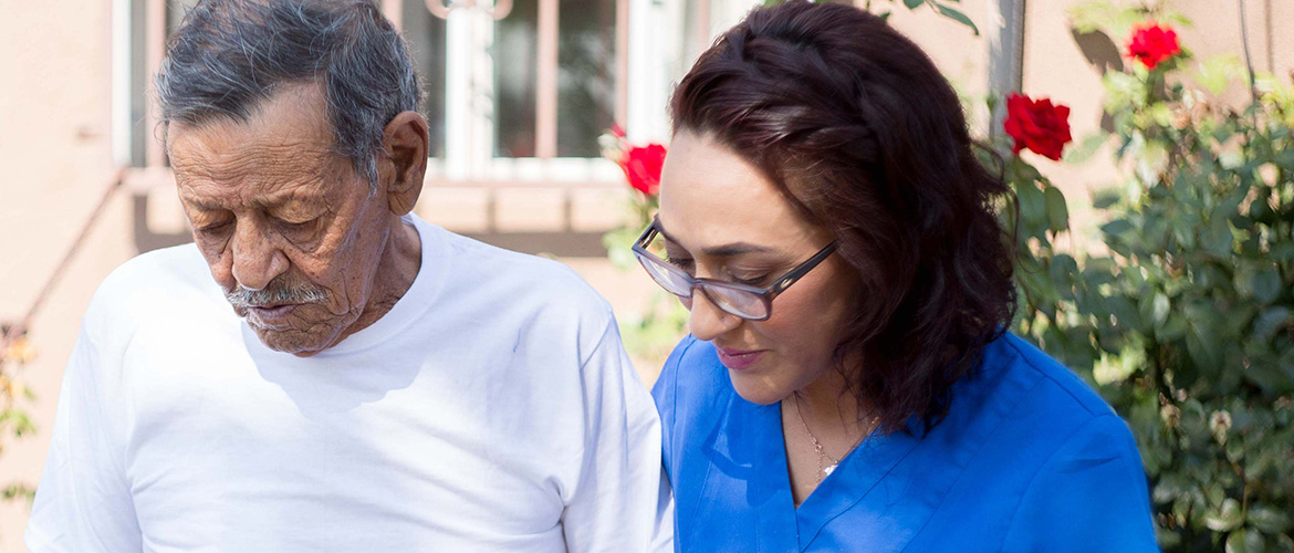 Young woman holds older man's arm as she assists him