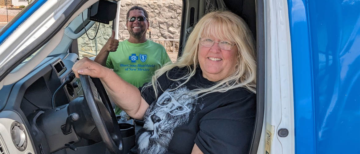 A woman sits in the driver's seat of a van while a smiling man gives through the passenger door behind her.