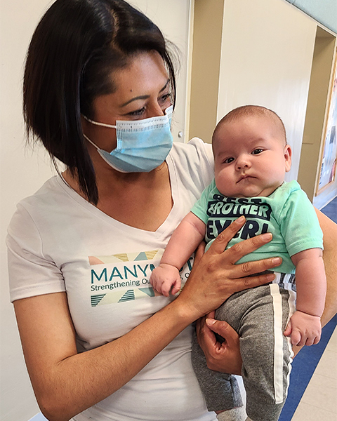 A volunteer wearing a Many Mothers T-shirt holds a baby.