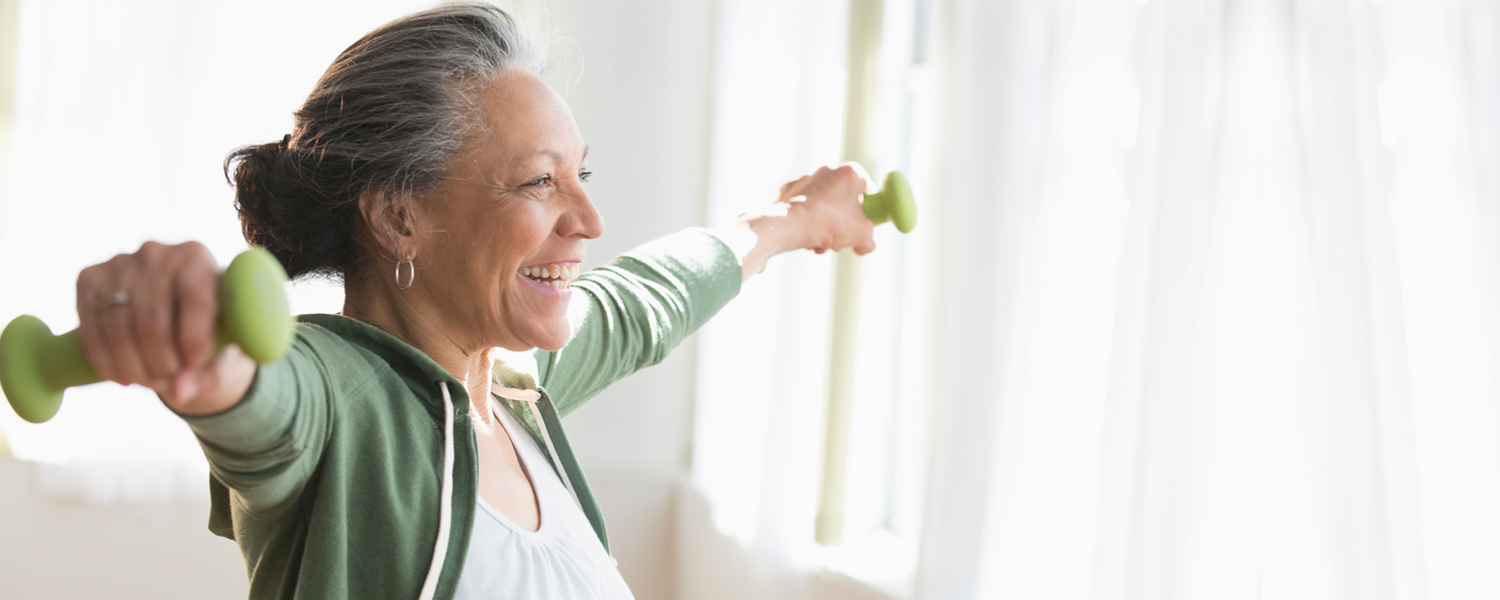 A woman smiles while working out with hand weights